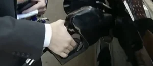 A person in a suit is holding a fuel nozzle at a gas pump.