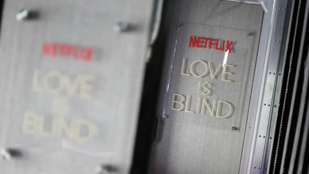 The image shows a close-up of a Netflix sign for the show "Love is Blind" displayed on a set or production area.