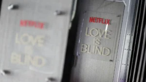 The image shows a close-up of a Netflix sign for the show "Love is Blind" displayed on a set or production area.