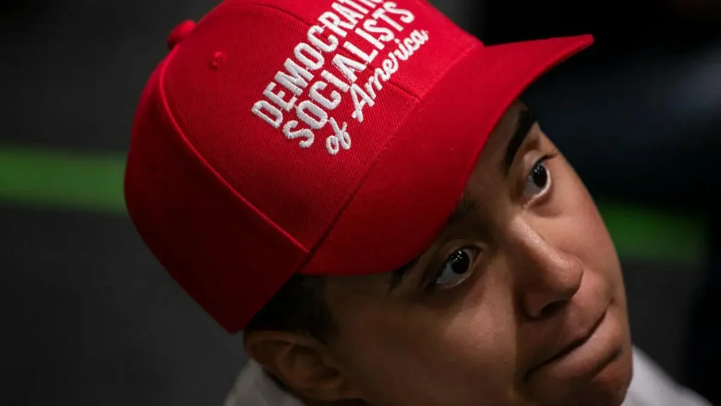 The image shows a person wearing a red cap with the text "Democratic Socialists of America" on it.