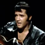 The image shows a person in a black leather jacket playing a guitar and singing into a microphone.