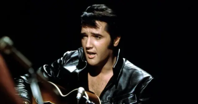 The image shows a person in a black leather jacket playing a guitar and singing into a microphone.