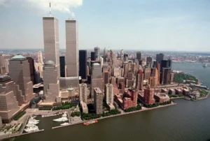 The image shows a panoramic view of the New York City skyline, featuring the iconic Twin Towers and surrounding skyscrapers, with a body of water in the foreground.