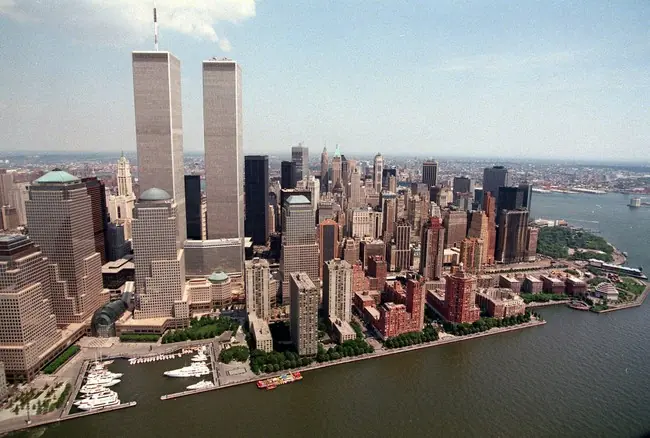 The image shows a panoramic view of the New York City skyline, featuring the iconic Twin Towers and surrounding skyscrapers, with a body of water in the foreground.