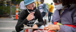 A volunteer wearing a "VOTE" shirt assists a person with voter registration at an outdoor event.