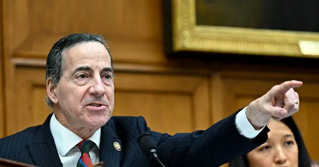 A man in a suit and tie is gesturing with his right hand while speaking at a podium.