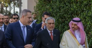 The photo shows a group of men in formal attire, including suits and traditional attire, walking together outdoors.