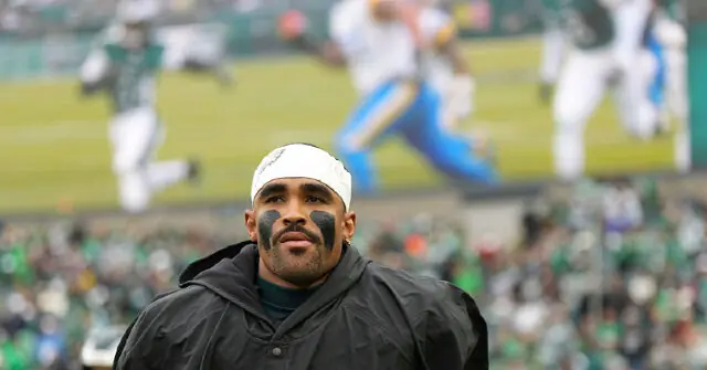 A football player wearing a headband and face paint stands on the sidelines during a game.