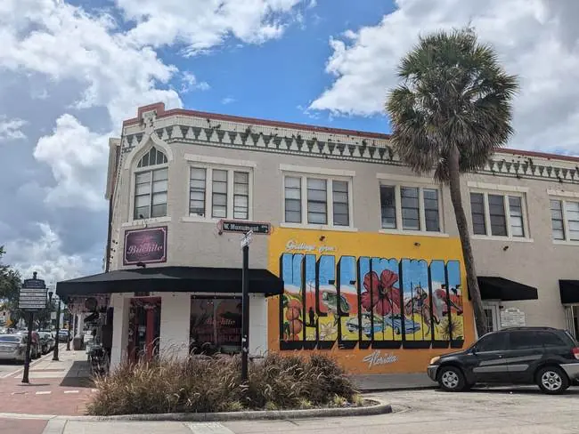 A vibrant mural adorns the side of a historic building in a sunny, urban setting.