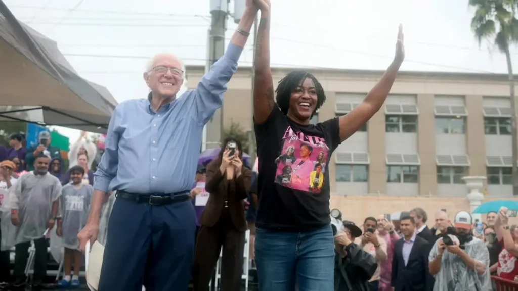 Two individuals raise their arms in celebration at an outdoor event, surrounded by a crowd of onlookers.
