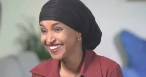 The image shows a person wearing a black head covering and a red top, smiling warmly.