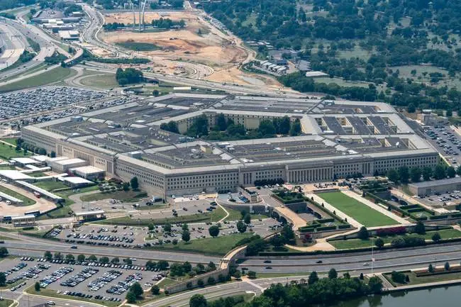 The image shows an aerial view of the Pentagon, a large five-sided building located in Washington, D.C., surrounded by roads, parking lots, and greenery.