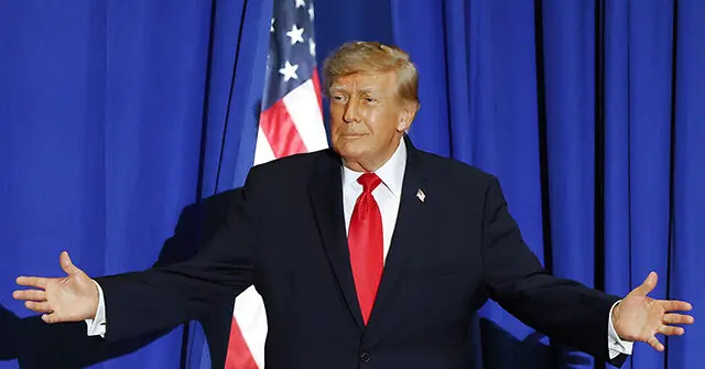 The image shows a person in a suit with an American flag in the background, gesturing with their hands outstretched.