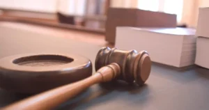 A judge's gavel rests on a table in a courtroom setting.