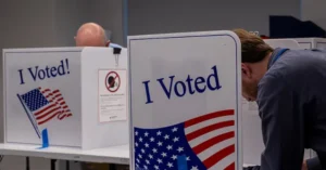 The image shows two individuals at voting booths with "I Voted!" signs featuring American flags, emphasizing the act of voting in the United States.