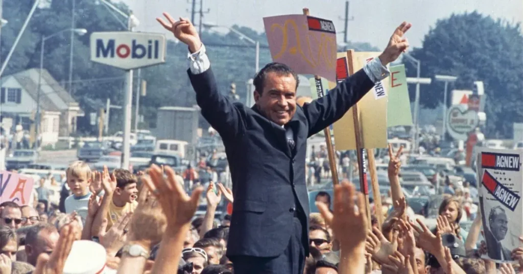 A politician raises his arms in victory as a crowd cheers and holds signs in support.
