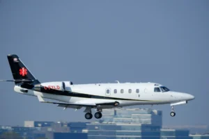 A medical aircraft with the registration C-FYLD is captured in flight, preparing to land against a backdrop of buildings.