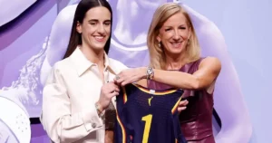 Two women are presenting a sports jersey with the number 1 on it, smiling and posing for the camera.