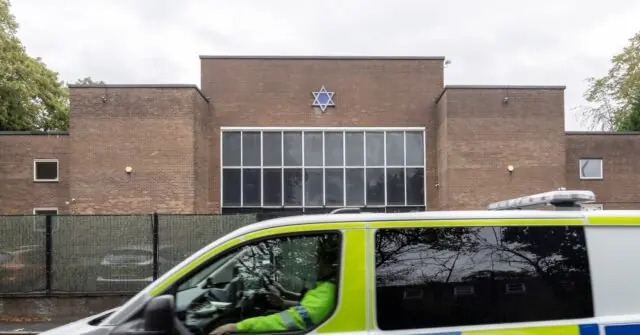 A police vehicle is parked in front of a brick building with a Star of David, indicating a Jewish community center.