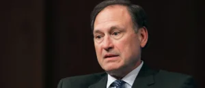 The image shows a man in a suit and tie, appearing to be in a formal or professional setting.