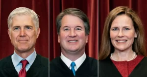 The image shows three individuals in judicial attire, likely representing Supreme Court justices, against a red curtain backdrop.