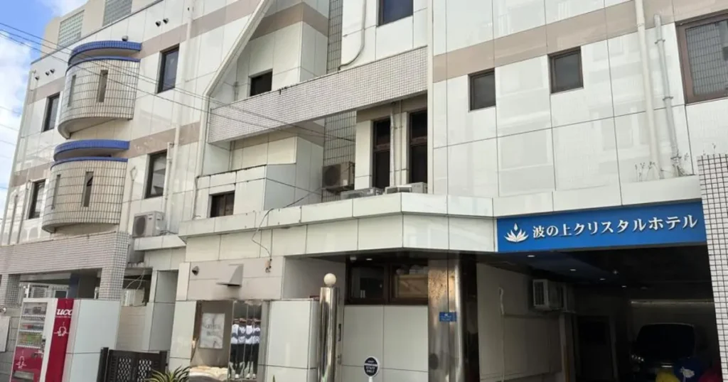 The image shows the exterior of the "Waves Crystal Hotel" in Japan, featuring a modern building with balconies and a blue sign with white text.