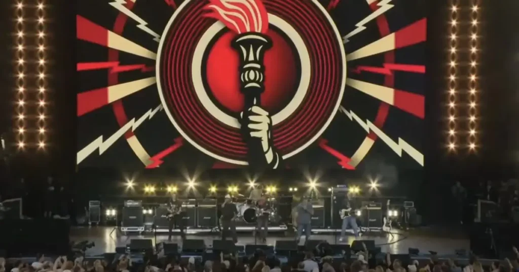 A band performs on stage with a vibrant, lightning-themed backdrop and enthusiastic audience in the foreground.