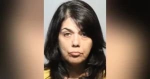 The image appears to be a mugshot of a woman with long dark hair, wearing a yellow top.