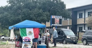 A group of people gather under a blue tent with a Mexican flag, promoting voter registration and other community activities near Davis Middle School.