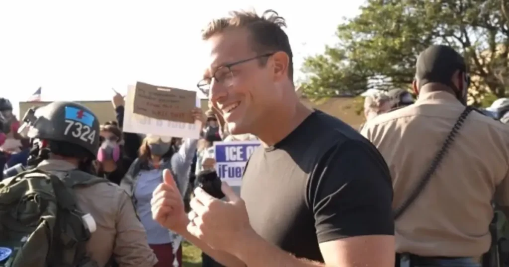 A man gives a thumbs-up while surrounded by protesters and law enforcement during a demonstration.