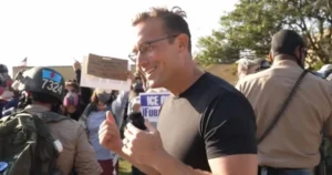 A man gives a thumbs-up while surrounded by protesters and law enforcement during a demonstration.