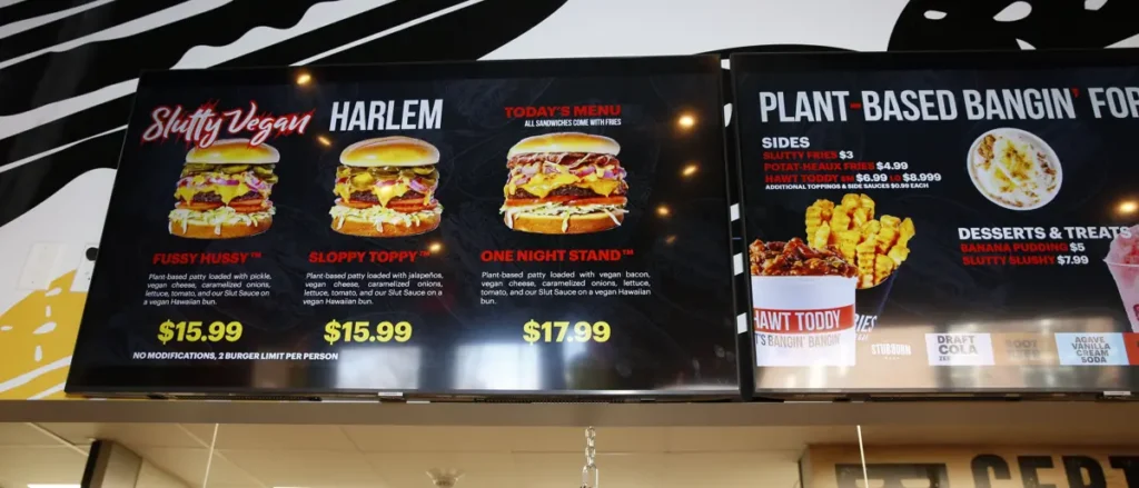 The menu board displays various plant-based burgers and sides at a vegan restaurant.