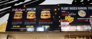 The menu board displays various plant-based burgers and sides at a vegan restaurant.