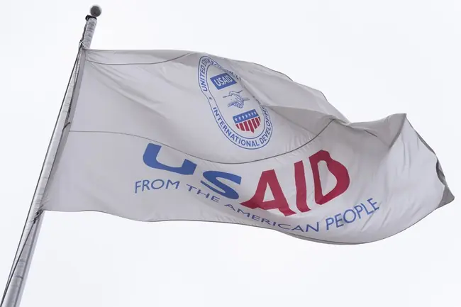 The photo shows a flag with the logo and text "USAID FROM THE AMERICAN PEOPLE" waving in the wind.