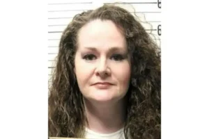 The image appears to be a mugshot of a woman with curly hair, taken against a background with a grid pattern.
