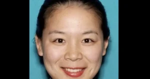 The image shows a person with a neutral expression against a solid blue background.