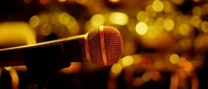 A close-up of a microphone against a backdrop of warm, bokeh-lit lights suggests a setting for a live performance or event.