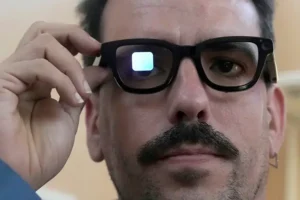 A person adjusts a pair of smart glasses, which reflect a small screen displaying a YouTube logo.
