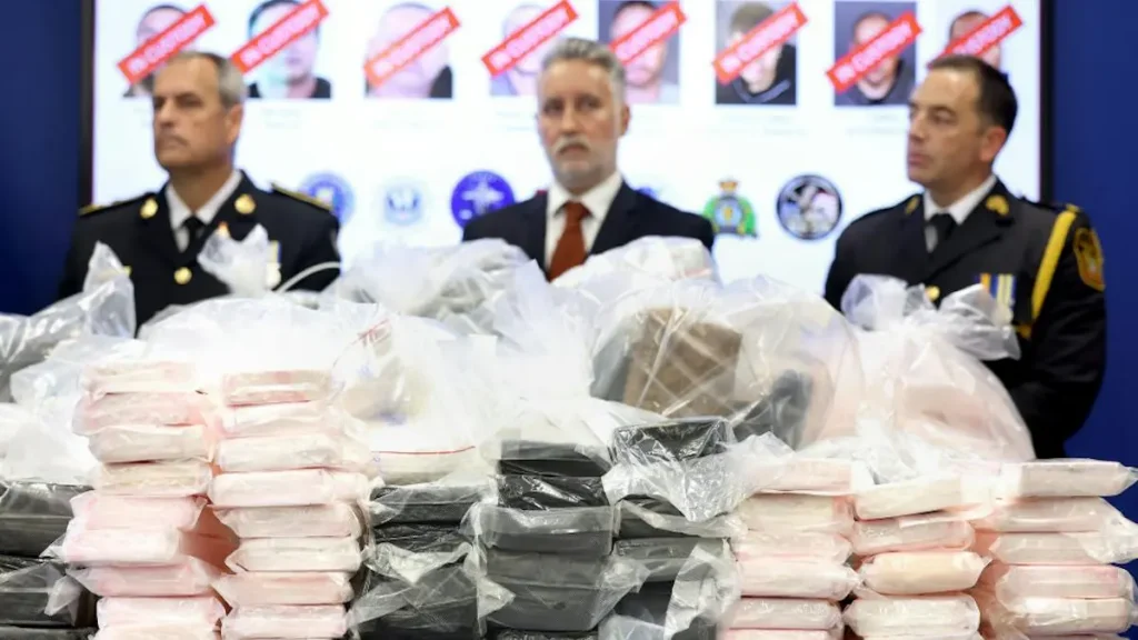 The photo shows law enforcement officials presenting a large quantity of seized packages, likely related to a drug trafficking operation.