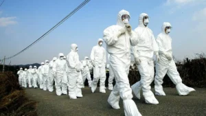 A group of individuals in white protective suits and masks are walking in a line, possibly during a training or emergency response exercise.
