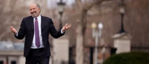 A man in a suit and tie stands with his arms outstretched in an outdoor setting.