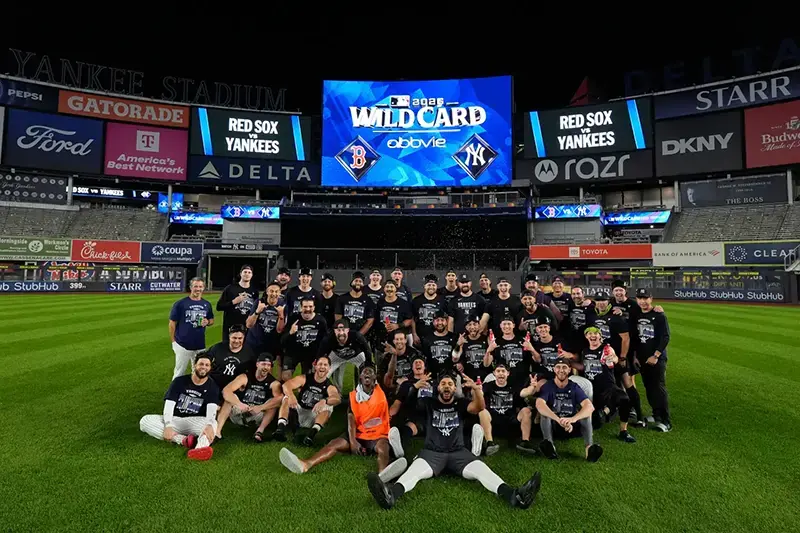 A group of baseball players and staff celebrate on the field at Yankee Stadium during a Wild Card game.