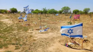 The image shows a memorial site with numerous Israeli flags planted in the ground, likely commemorating fallen soldiers or victims.