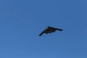 A stealth aircraft is captured flying against a clear blue sky.