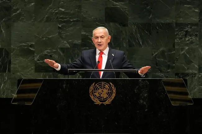 The image shows a man speaking at a podium with the United Nations emblem, indicating he is addressing the UN General Assembly.