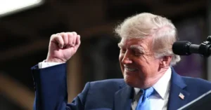The image shows a person in a suit and tie, raising their fist in a gesture of triumph or solidarity.