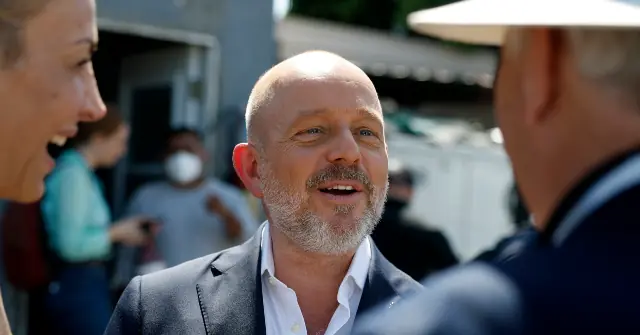 A man in a suit is engaged in conversation with two other individuals in an outdoor setting.