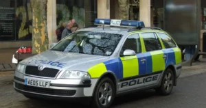 A police car with blue and yellow markings is parked on a street in an urban area.