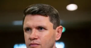 The image shows a close-up of a man with short, neatly styled hair, looking serious and focused.