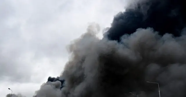The image shows a large plume of smoke rising into the sky, indicating a significant event or incident, possibly a fire or explosion.